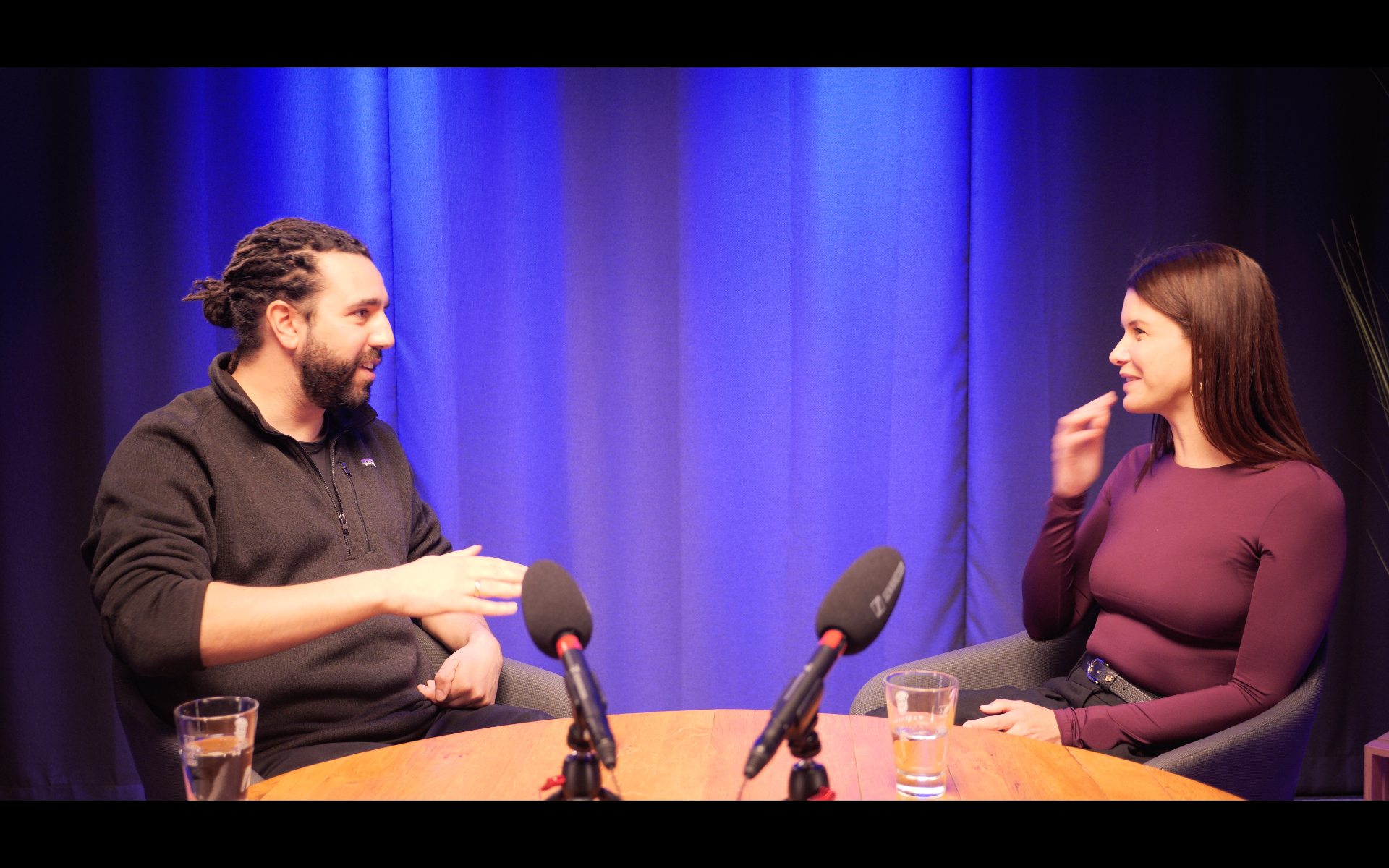 Business-Podcast im Prismeo Studio mit zwei Gesprächspartnern am runden Tisch vor blau beleuchtetem Hintergrund