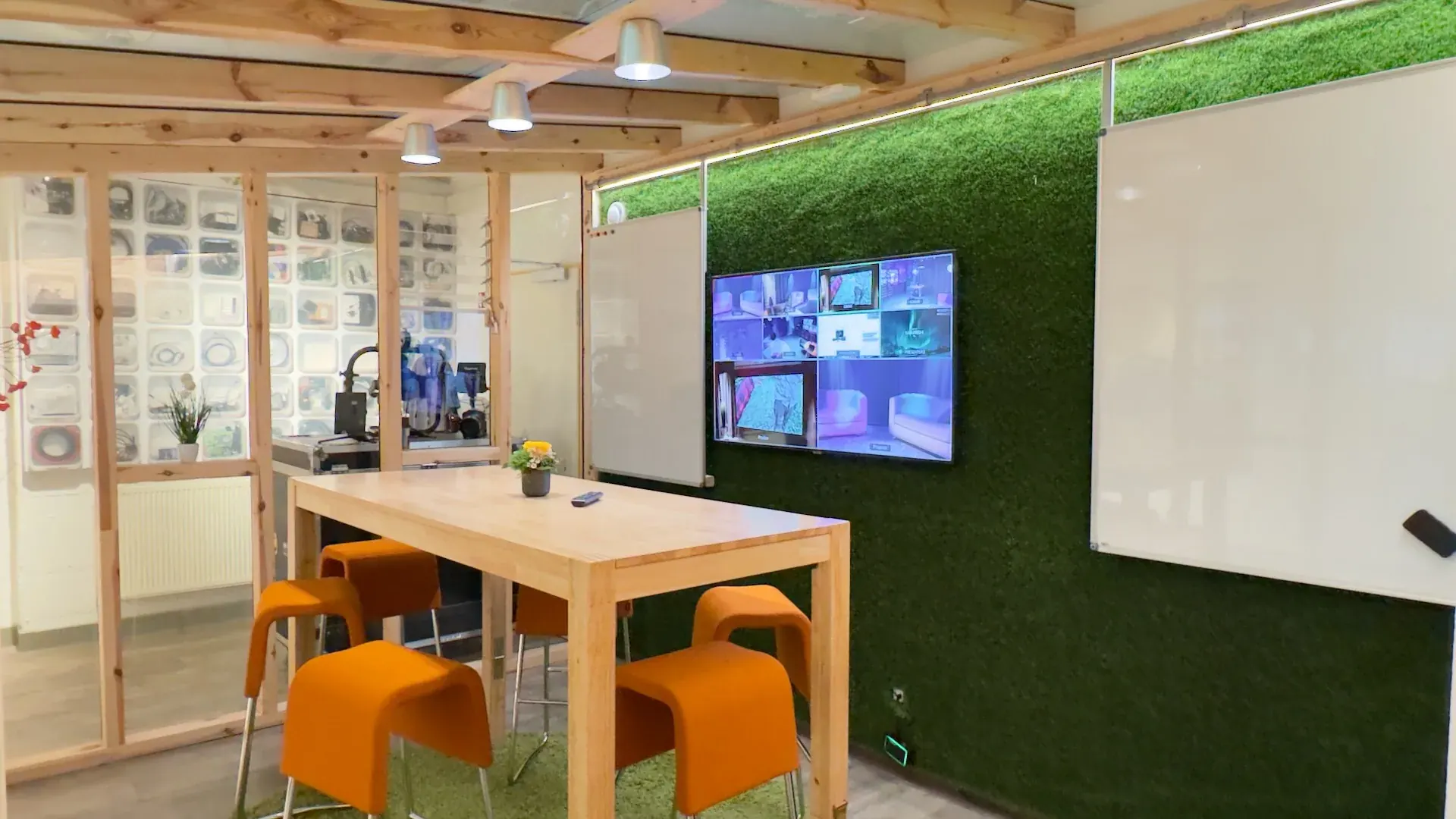Greenhouse – Holztisch mit orangefarbenen Hockern im Greenhouse, Mooswand und Multi-View-Display