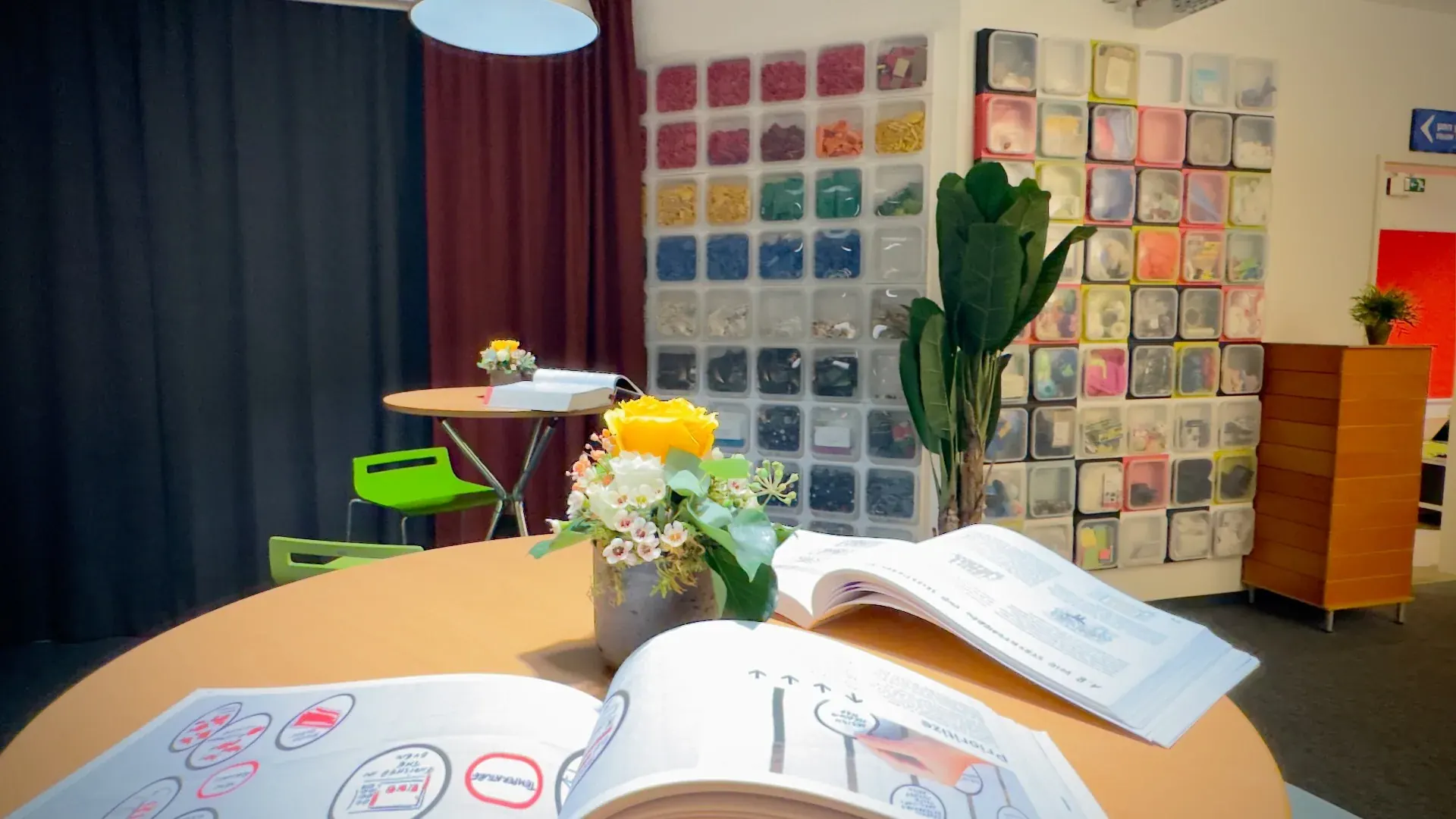 Idealab – Manual Thinking Workshop-Tisch im Idealab mit Büchern, Blumen und Materialwand im Hintergrund