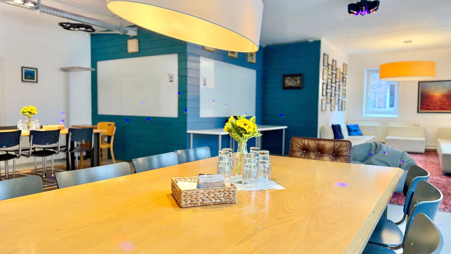 Loft – Großer Workshop-Tisch im Loft mit Whiteboards, Sonnenblumen, Gläsern und Blick in den Lounge-Bereich