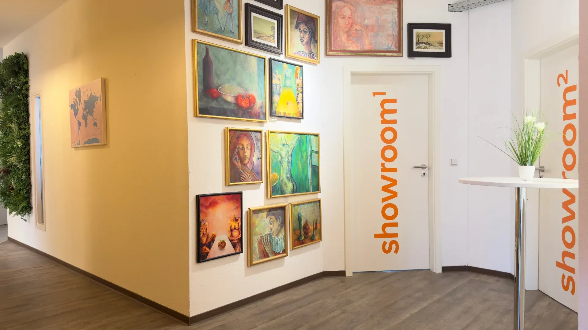 Showroom – Eingangsbereich zum Showroom im Prismeo LAB mit Gemäldegalerie, grüner Pflanzenwand und orangefarbenem showroom-Schriftzug an der Tür