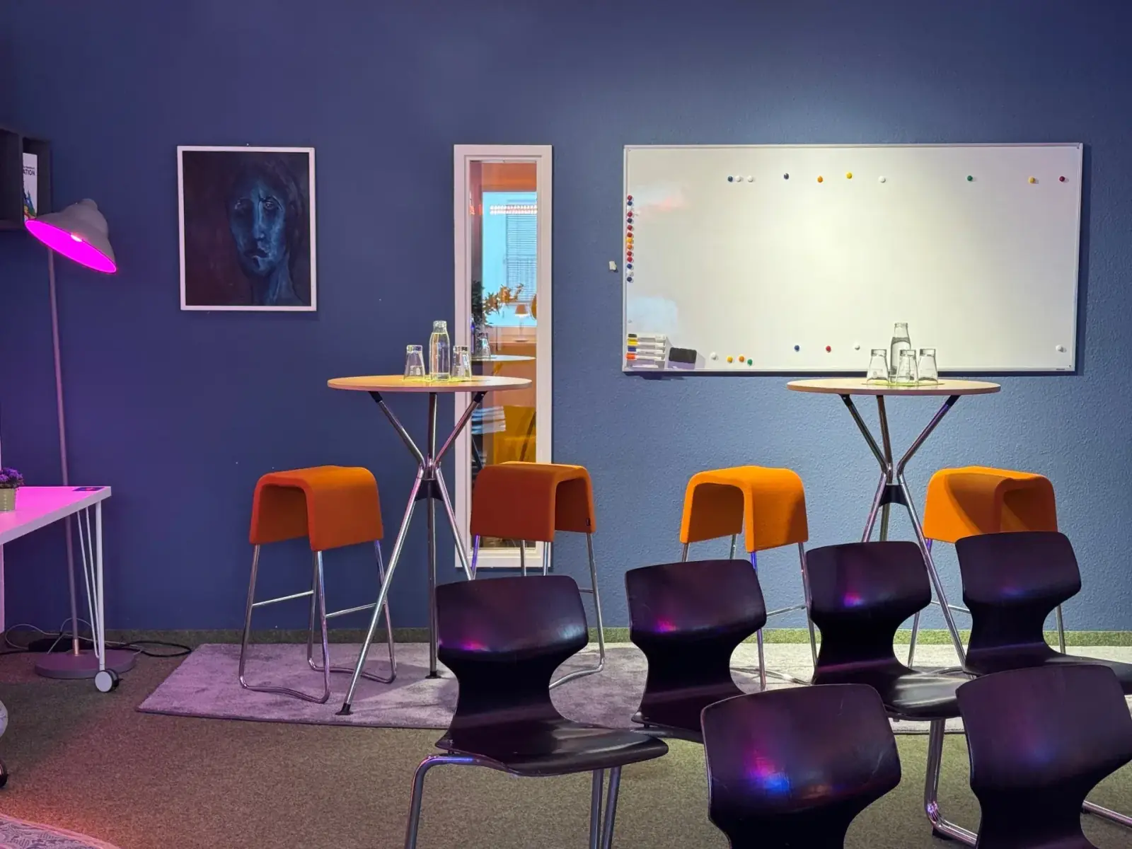 Showroom – Showroom im Prismeo LAB mit Stehtischen, orangen Hockern und Reihenbestuhlung vor Whiteboard