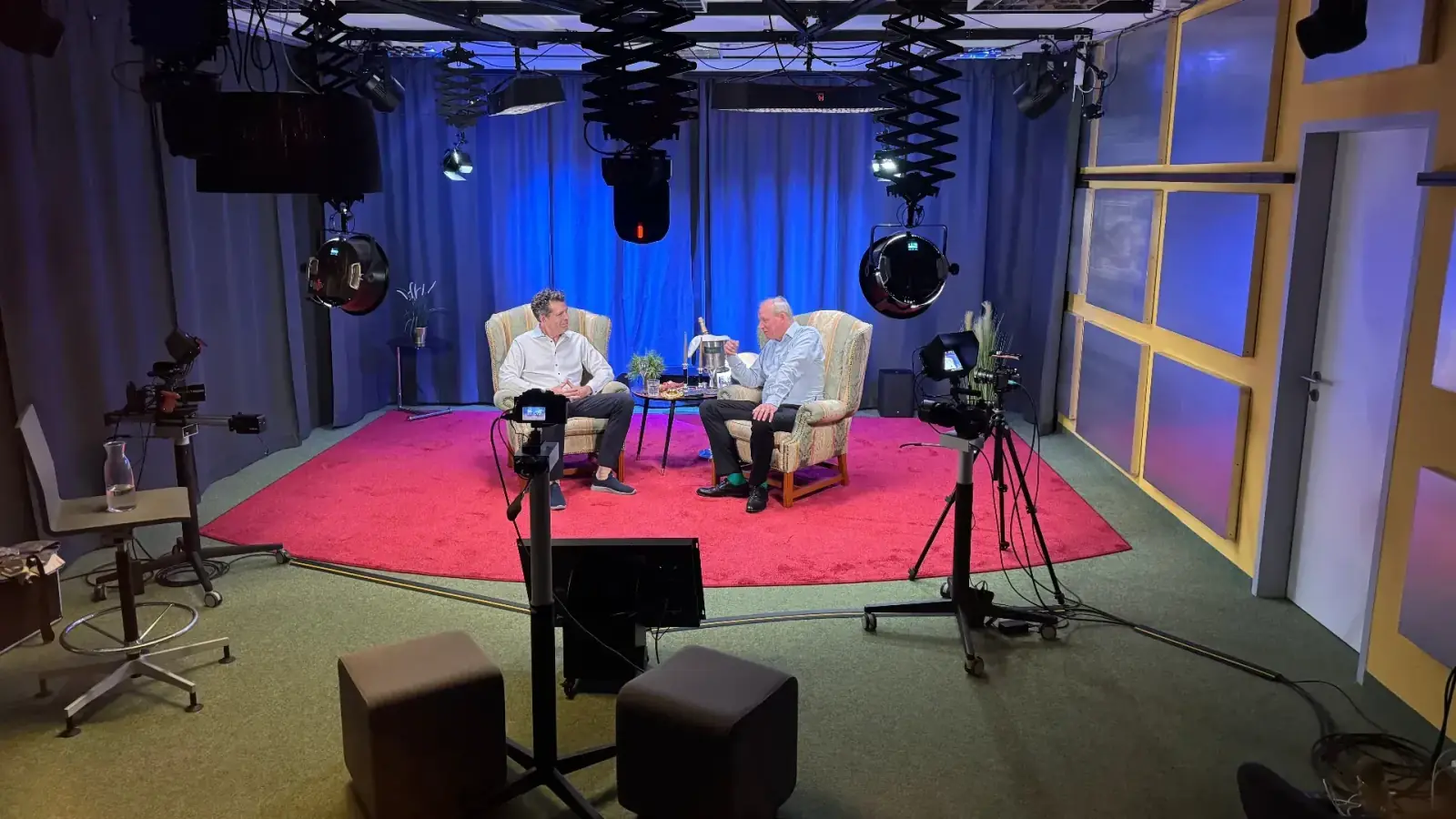 Theater – Talkshow-Setup im Theater des Prismeo LAB mit zwei Sesseln auf rotem Teppich, blauer Vorhangkulisse und professioneller Kamera- und Lichttechnik