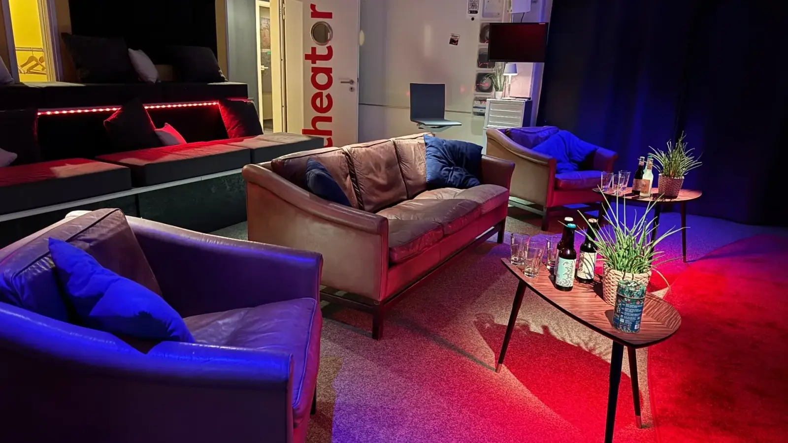 Theater – Lounge-Bereich im Theater mit Ledersofas, Beistelltischen und farbiger LED-Beleuchtung