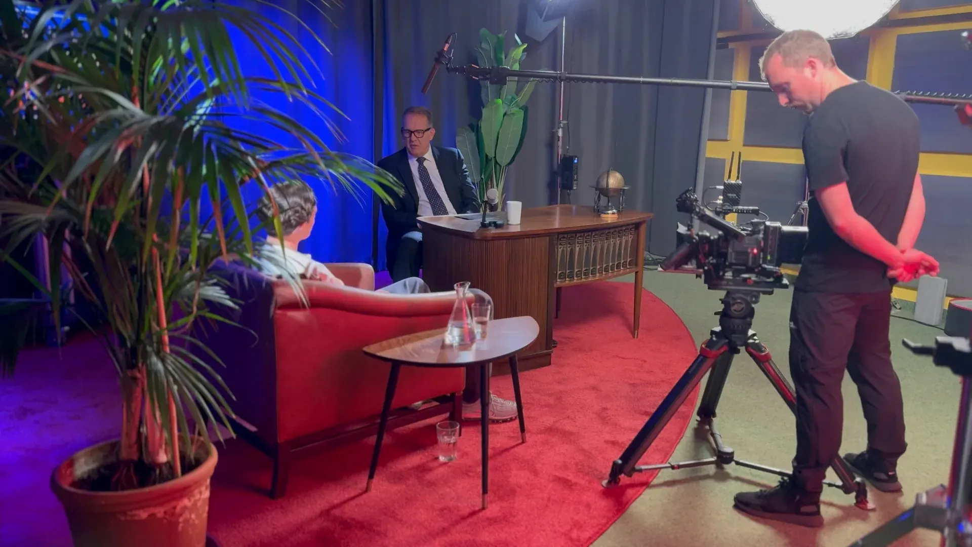 Theater – Weitwinkelansicht einer Talkshow-Produktion im Theater mit Moderator, Gast, Pflanzen und professionellem Kamera-Setup