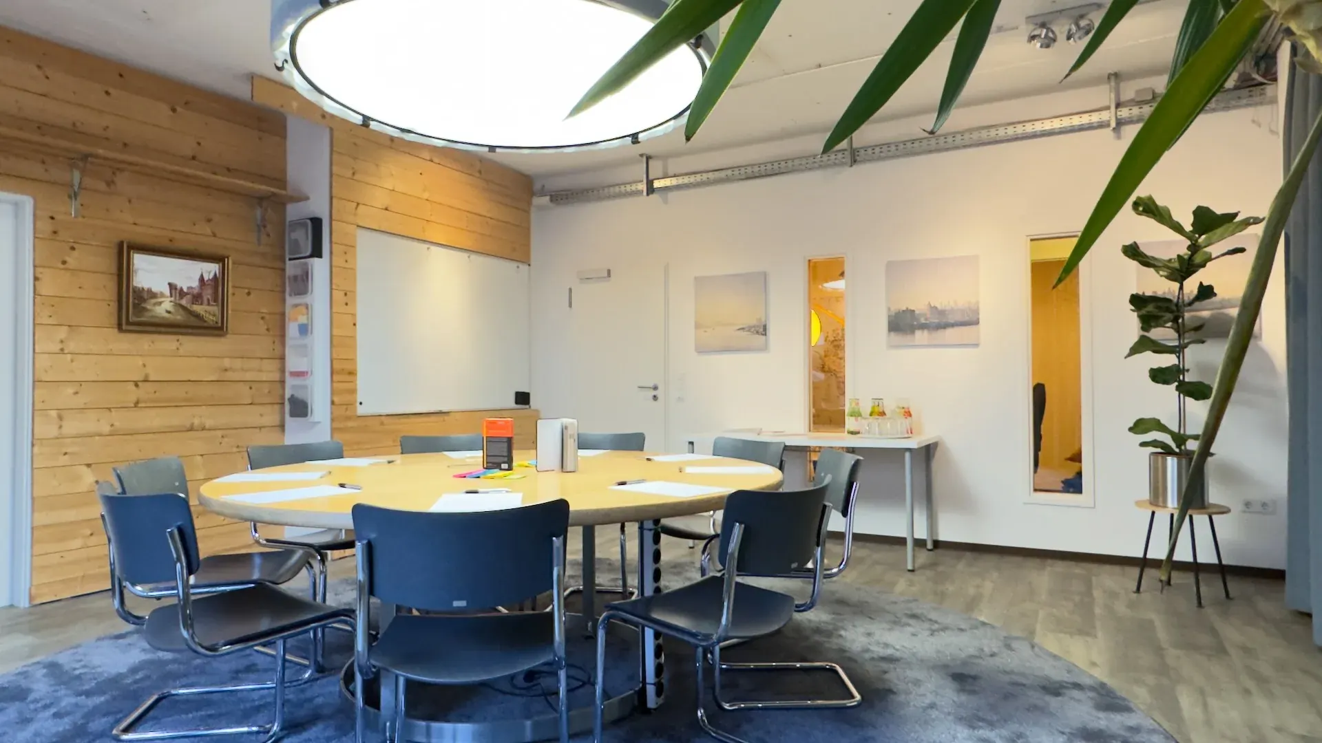 Thinktank – Seitenansicht des Thinktank mit rundem Tisch, Whiteboard, HafenCity-Bildern und Tageslicht