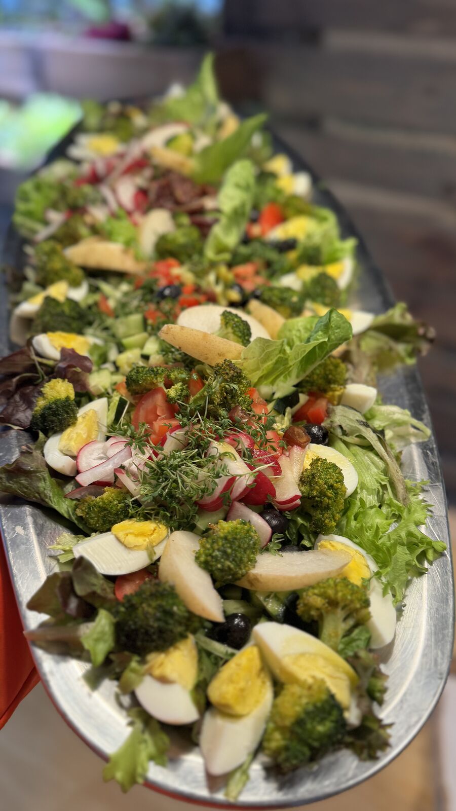 Große Platte mit vielseitigem Salat, hartgekochten Eiern, Brokkoli, Radieschen und schwarze Oliven angerichtet.