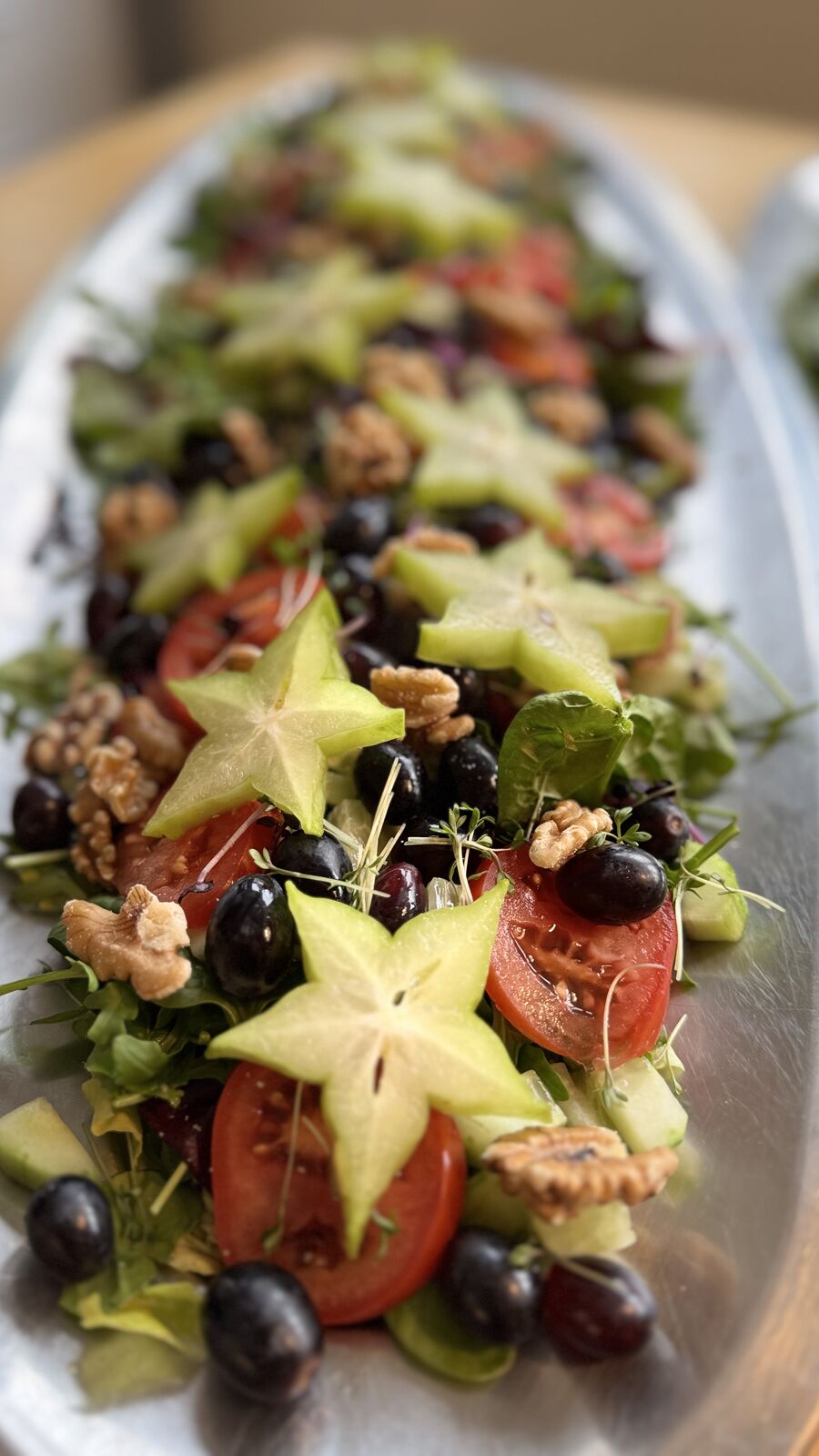 Bunter Salat mit Sternfrucht, Tomaten, Weintrauben und Walnüssen auf einer Servierplatte.