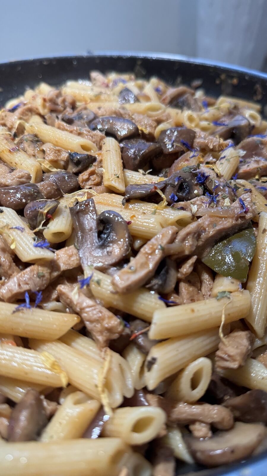 Nudeln mit Pilzen, grünem Gemüse und Fleischstreifen in einer Pfanne.