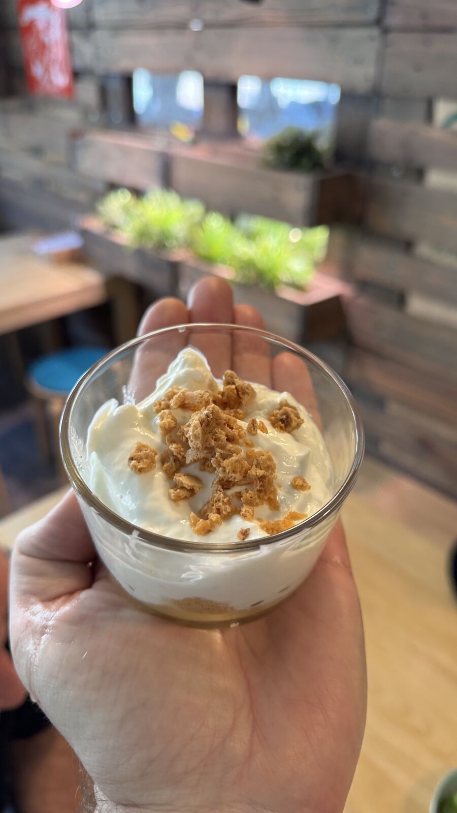 Dessert im Glas mit Creme und Keksstreuseln, in der Hand gehalten