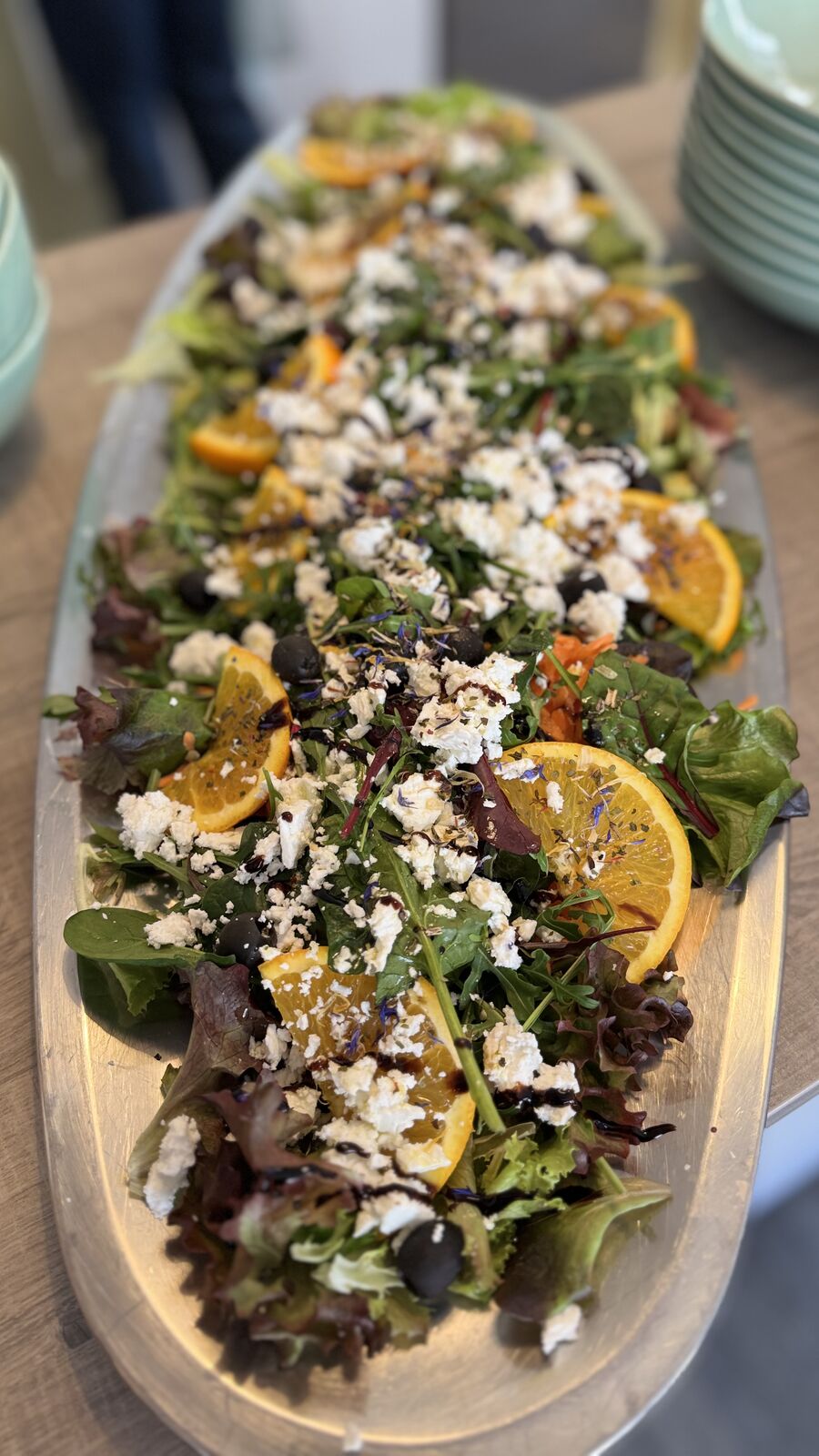 Langer Servierteller mit Blattsalat, Feta, Orangen und Oliven.
