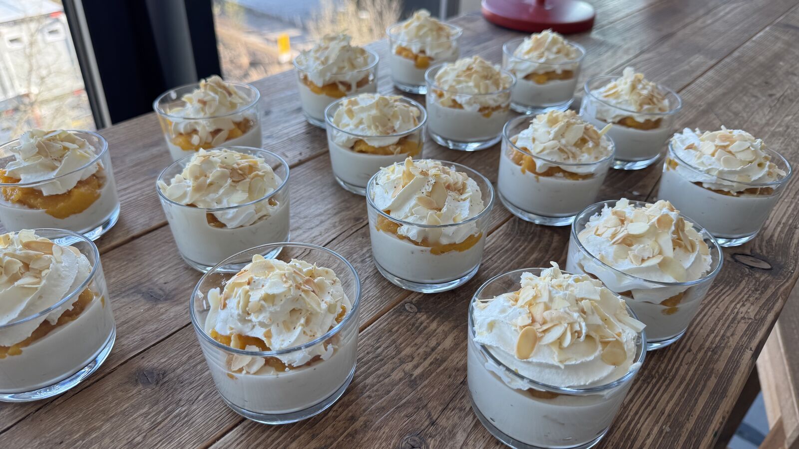 Dessert-Gläschen mit weißer Creme, Fruchtpüree und Mandelblättchen auf Holzoberfläche