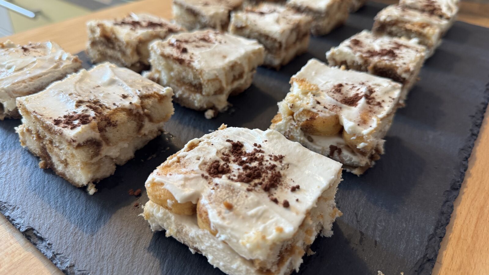Rechteckige Stücke Tiramisu mit Kakaopulver auf dunkler Platte