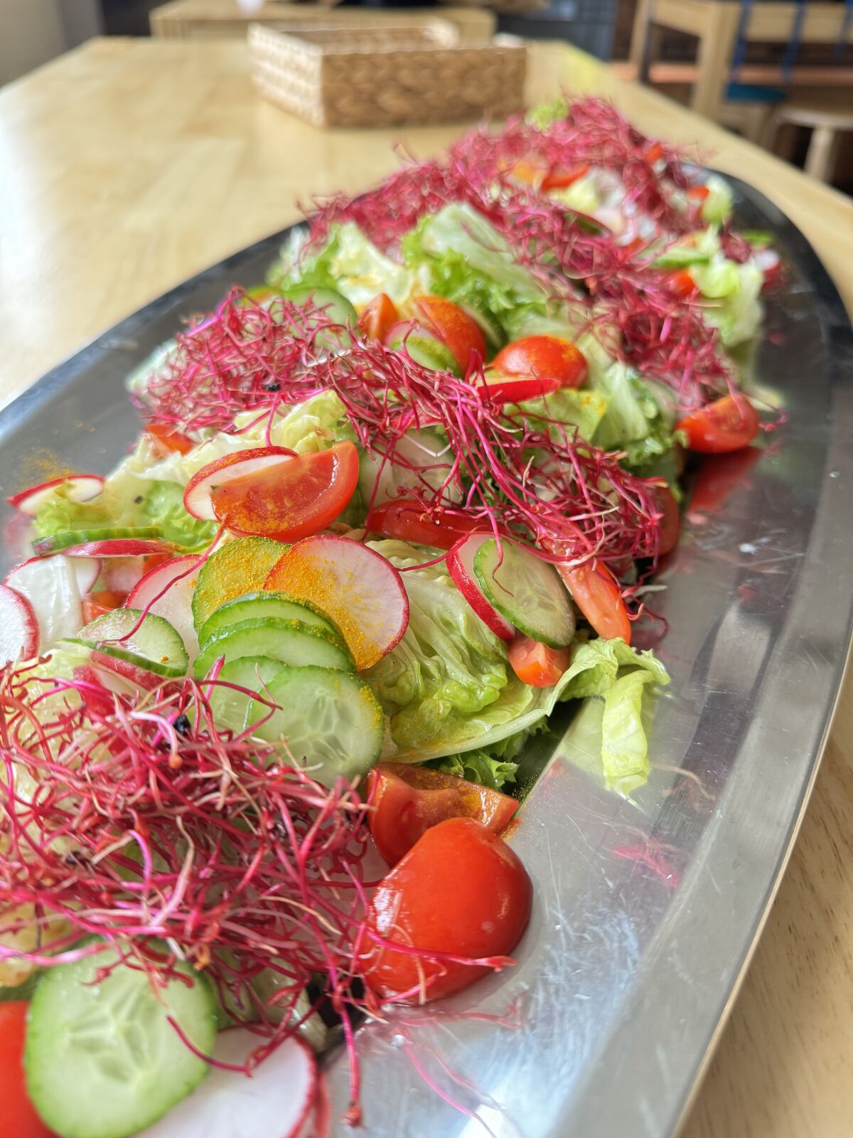 Bunter Salat angerichtet auf einer länglichen Platte mit Keimlingen garniert.