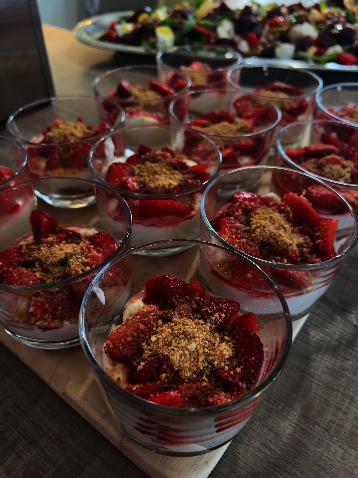 Dessertbecher mit Erdbeeren und Keksstreuseln, im Hintergrund Salatteller.