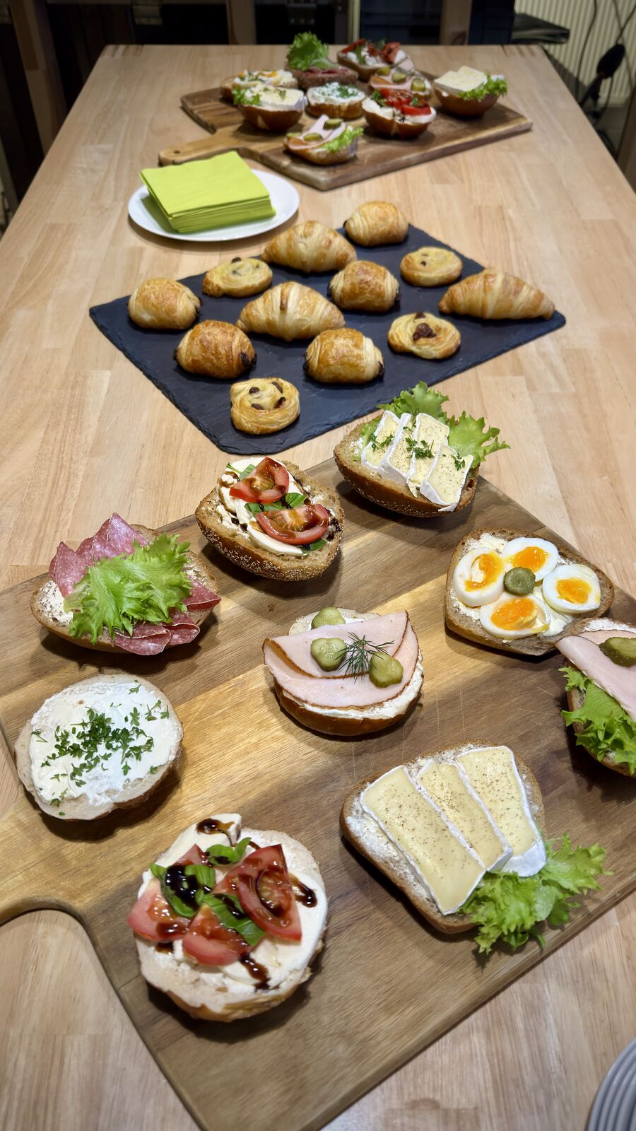 Brötchen und Croissants auf Holzbrettern und schwarzer Platte, appetitlich angerichtet.