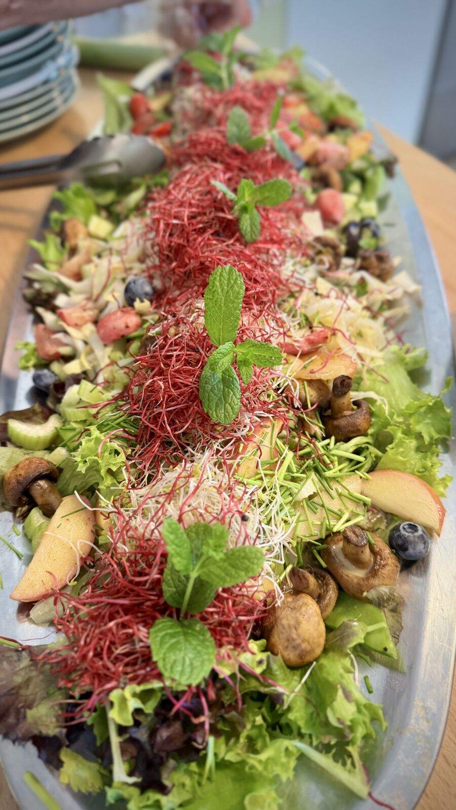 Buntes Salatbuffet mit Pilzen, Früchten und Sprossen, garniert mit Minze auf ovaler Servierplatte.