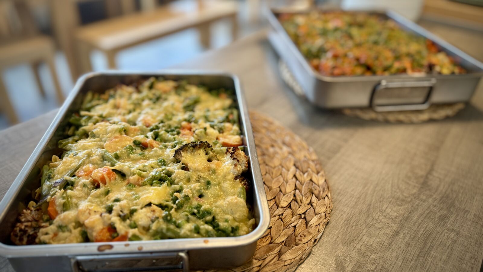 Zwei Auflaufformen mit überbackenem Gemüse und Käse auf einem Tisch.