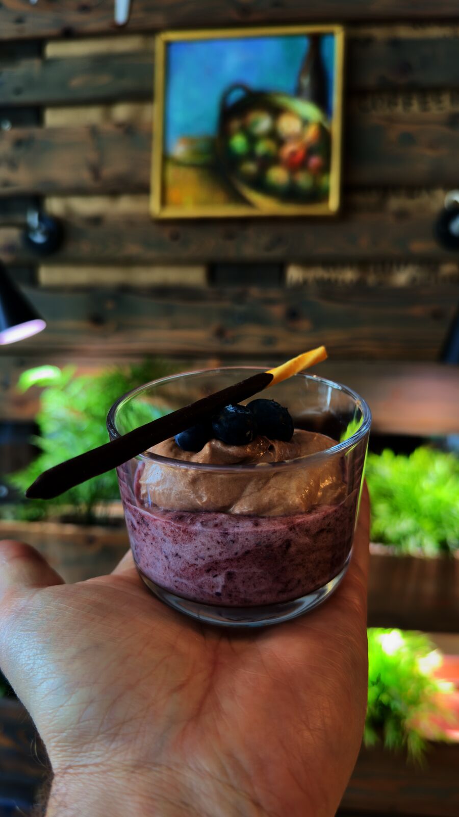 Dessert aus Blaubeer- und Schokoladenmousse im Glas, von einer Hand gehalten.