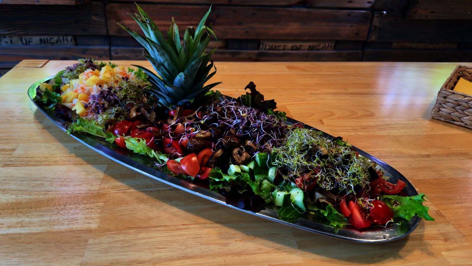 Längliche Platte mit Salat, Sprossen, Pilzen, Tomaten und Ananas auf Holzplatte angerichtet.
