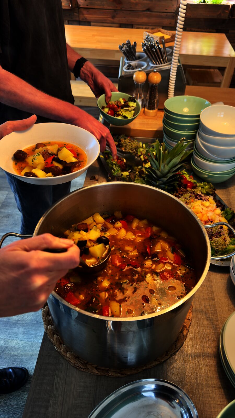 Person schöpft Eintopf und nimmt sich weitere Speisen vom Buffet