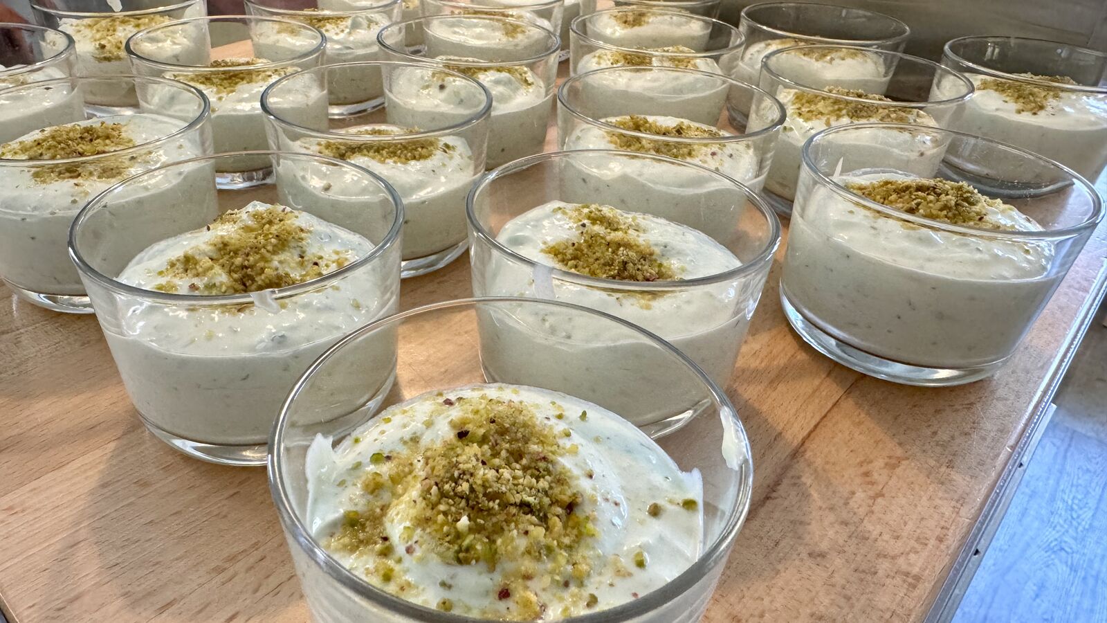Reihen von Pistazien-Desserts in Gläsern auf einem Holztisch, bereit zum Servieren.