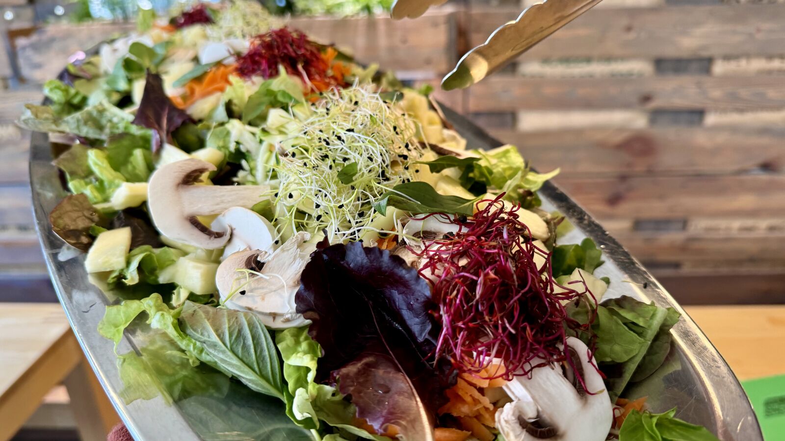 Großer Salat mit Blattsalat, Pilzen, Sprossen und bunten Gemüsesorten in einer Servierplatte.