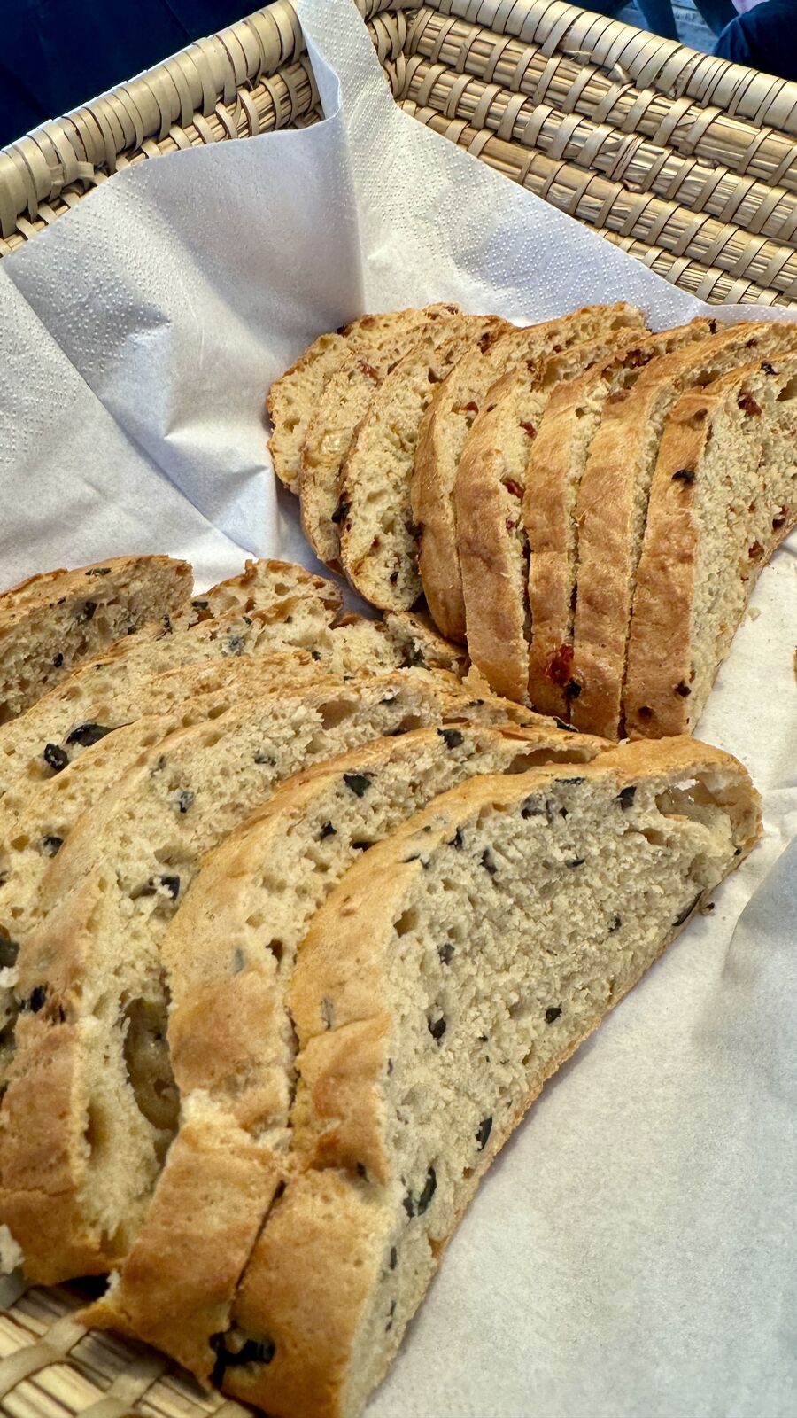 Zwei Brote, eines mit Oliven, eines mit Tomaten, in Scheiben geschnitten in einem Brotkorb