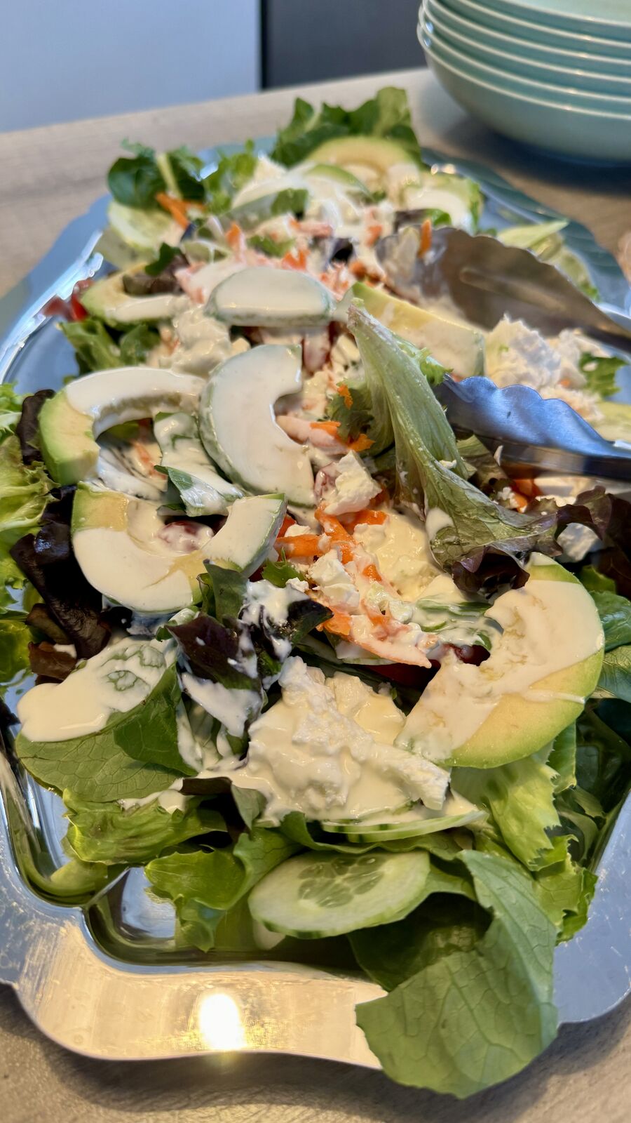 Bunter Salat mit Avocado, Karotten und cremigen Dressing auf silberner Servierplatte.