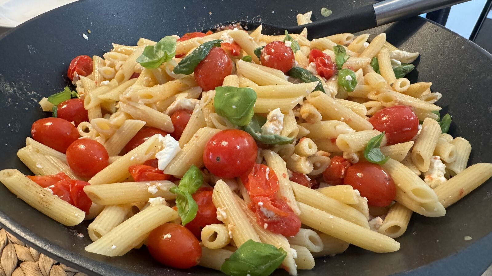 Penne Nudeln mit Kirschtomaten, Feta und Basilikum in einer schwarzen Wok-Pfanne