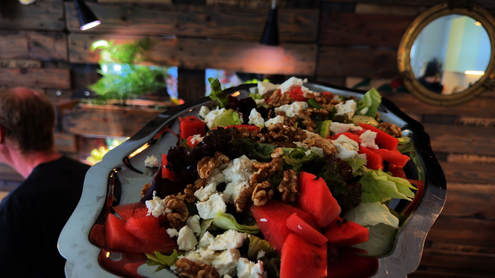 Wassermelonen-Feta-Salat mit Walnüssen in einer Servierplatte, im Hintergrund Schemen eines Mannes.