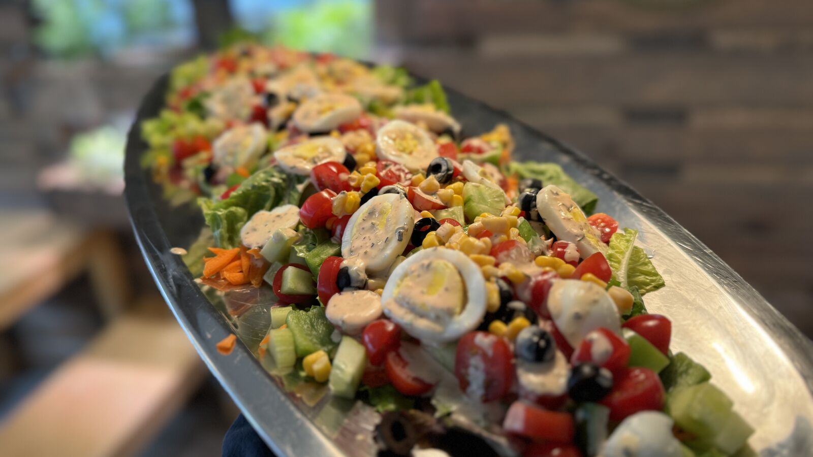 Buntes Salatbuffet mit Eiern, Oliven, Mais und frischem Gemüse auf einer Servierplatte.